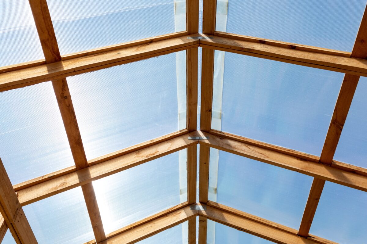 Dach eines Gewächshauses, einer Scheune oder eines anderen landwirtschaftlichen Gebäudes bestehend aus transparentem Polycarbonat und Holzbrettern.