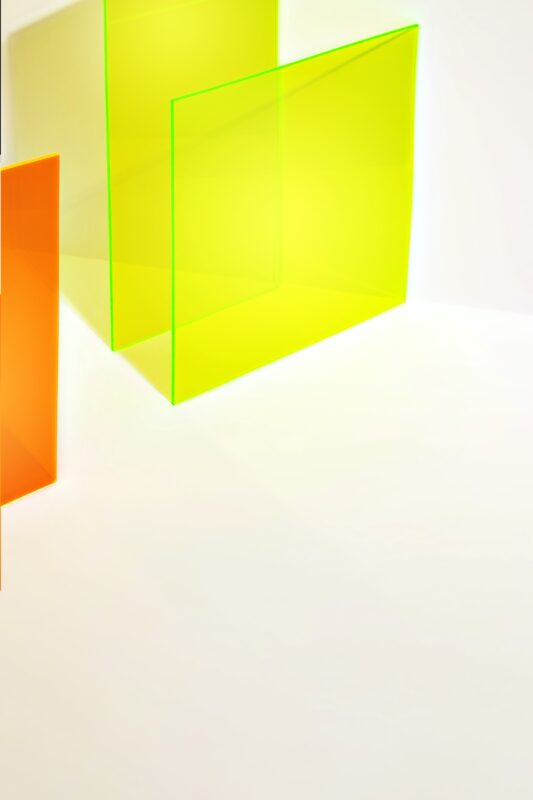 Fotografie eines orangefarbenen und neongelben Acryls, Plexiglas, mit Schatten auf weissem Hintergrund. Stilvoller geometrischer Hintergrund. Werbung, Kunst